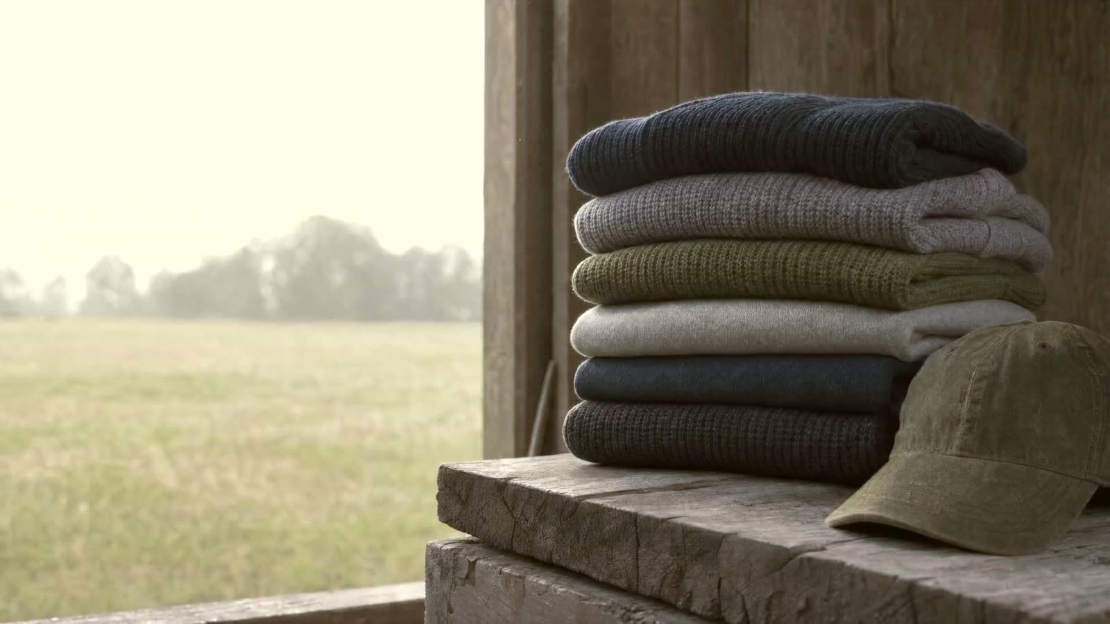 Rooted Label hero poster: gestapelde sweaters op een houten werkbank